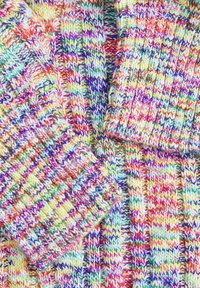 Tissu tricoté multicolore avec une texture côtelée, présentant des fils jaunes, rouges, violets, verts et bleus en gros plan.