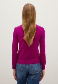Fuchsia Pullover mit langen Ärmeln und gerippten Bündchen, kombiniert mit blauen Jeans. Der Pullover hat ein enganliegendes Design und eine weiche Textur.