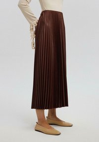 Brown pleated midi skirt with a smooth texture and elastic waistband, paired with beige flat shoes. Sleeves feature decorative fringe accents.