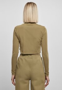 Olivenfarget, langermet croppet topp laget av myk stoff, kombinert med matchende høye bukser med elastisk midje og sidelommer.