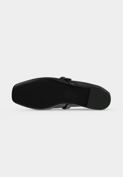 Chaussure noire vue de dessous, mettant en valeur sa semelle lisse et son bout carré sur un fond uni clair.