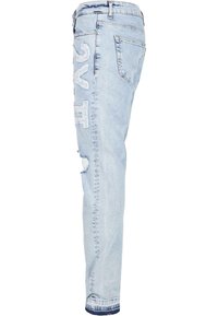 Jeans en denim bleu clair avec une coupe slim, présentant des détails déchirés et une broderie sur le côté. Design classique à cinq poches.