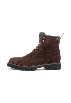 Bottines en daim marron avec bout rond, laçage à l'avant et œillets en métal. Dotées d'une semelle en caoutchouc avec un talon robuste. Anse à l'arrière.