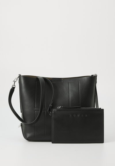 Schwarze Leder-Tote mit vertikalen Nähten und einem abnehmbaren Reißverschluss-Etui. Sie verfügt über einen verstellbaren Schultergurt und eine glatte Textur.