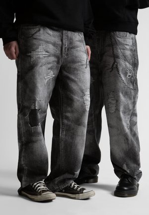 Dve osoby v voľných, opotrebovaných čiernych a sivých rifle s reťazovými doplnkami a čiernou obuvou, stojace vedľa seba.