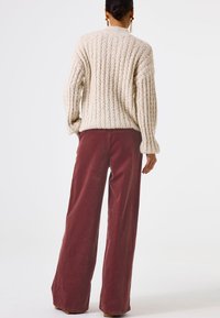 Jersey de punto con canalé en color crema y corte oversize, combinado con pantalones de pana sueltos en color burdeos. Ambos prendas tienen un aspecto texturizado.
