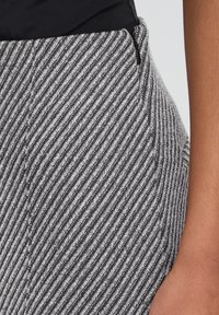 Gråt og hvidt stribet stof med en glat tekstur. Indeholder en side-lynlås og en tætsiddende pasform, del af et par skræddersyede bukser.