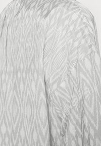Tessuto leggero e grigio con un sottile motivo ikat; presenta una vestibilità ampia e spalle scese per una silhouette rilassata.