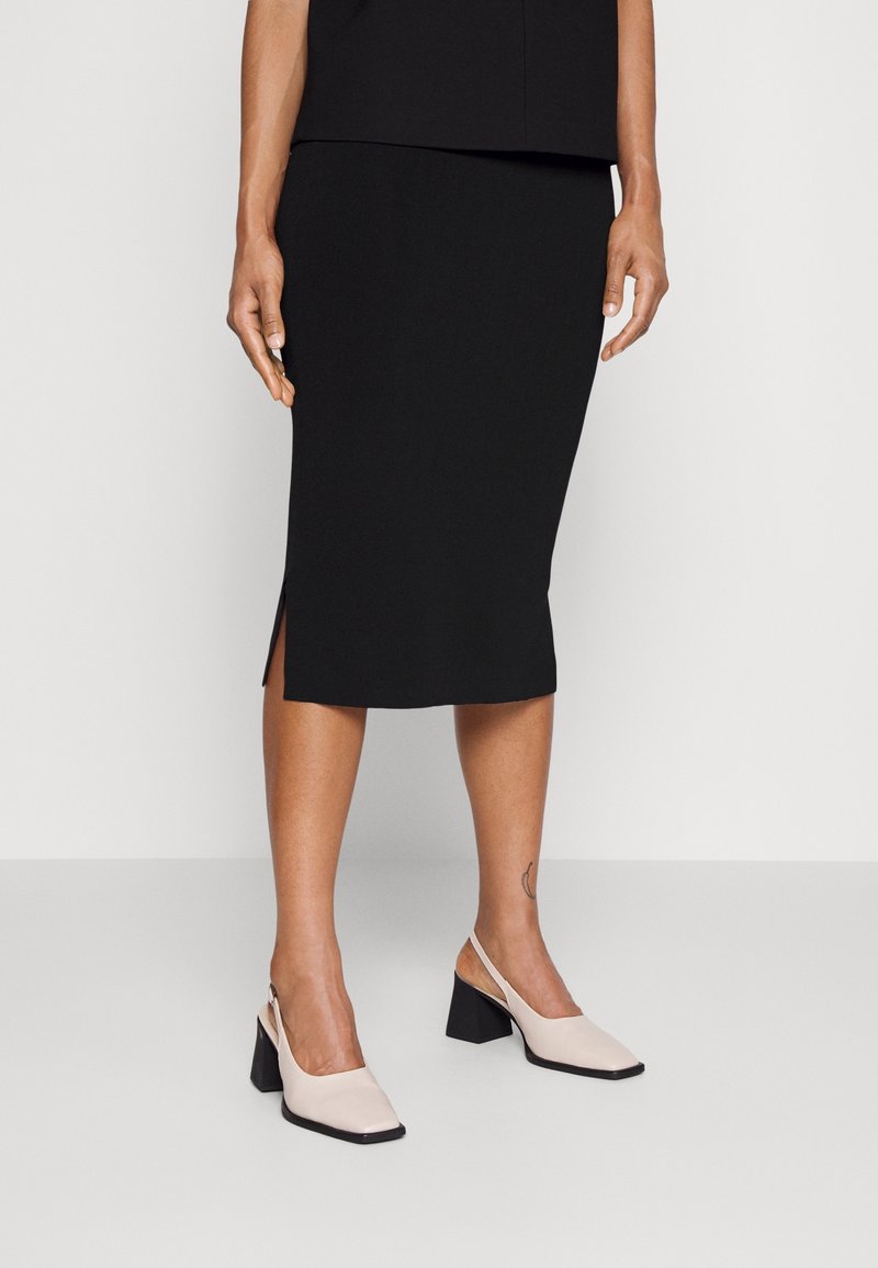 Mustahdud musta seeliku, millel on külgsuine lõhik; kombineeritud heledate roosade slingback-kontsadega, millel on ruudukujuline varvas ja paks must konts.