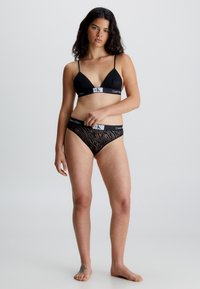 Set di lingerie nera composto da un bralette con spalline sottili e un bikini abbinato. Il bralette presenta un elastico con il logo Calvin Klein e un motivo texturizzato.