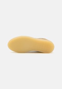 Gummisåle med strukturert grep, hovedsakelig beige farge, med en fleksibel, avrundet form og en glatt overflate.