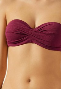 Haut de bikini sans bretelles bordeaux en tissu texturé, avec un design avant torsadé. Fini lisse, adapté à un usage en maillot de bain.