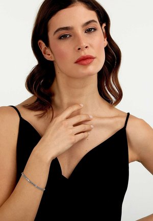 Silberarmband mit kleinen blauen und klaren Edelsteinen, am Handgelenk getragen, das ein zartes Design auf einem schwarzen Oberteil präsentiert.