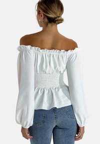 Weiße schulterfreie Bluse mit Rüschensaum am Hals, langen Ärmeln und gerafftem Taillenbereich. Glatter Stoff mit puffigen Ärmeln und einem Peplum-Design.