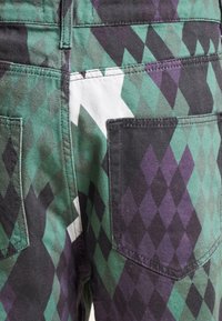 Black, green, and purple patterned pants with a diamond motif, featuring two back pockets and stitched seams. Cotton blend fabric with texture.