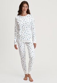 Witte loungewear-set met lange mouwen en een broek, voorzien van een kleurrijk winterthema-print van bomen en skiërs. Zachte stof met geribbelde manchetten.
