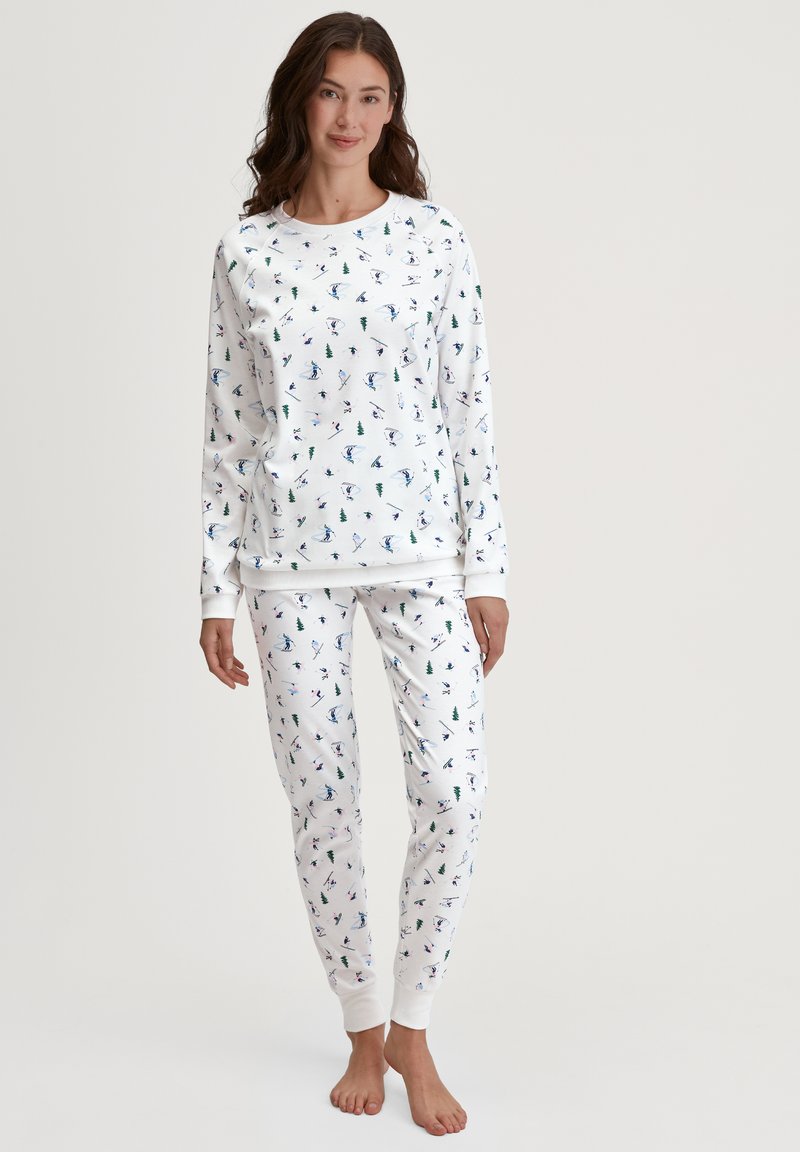 Witte loungewear-set met lange mouwen en een broek, voorzien van een kleurrijk winterthema-print van bomen en skiërs. Zachte stof met geribbelde manchetten.