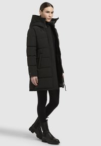 Melna, pamatota ziemas jaka ar augstu apkakli, rāvējslēdzēja aizdari un sānu kabatām. Jaka ir veidota ar plūstošu siluetu.