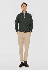 Ciemnoszary sweter z rozpięciem na szyi, beżowe spodnie oraz brązowe zamszowe botki za kostkę. Outfit charakteryzuje się casualowym stylem i dopasowanym krojem.