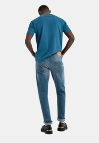Camiseta de algodón azul y jeans de un azul claro con un parche de cuero en la parte trasera. Zapatos negros con suela gruesa y puños remangados en los jeans.