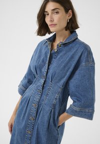 Džinsist kleit, millel on nööpidega esitükk, krae ja lühikesed varrukad. Valmistatud sinisest džinsist, veidi laiem, küljetaskutega.