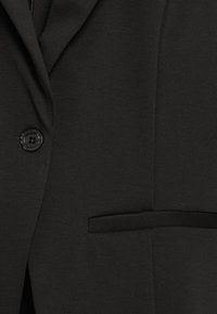 Svart blazer med enstaka knappknäppning, texturerad tyg och bröstficka med diskret sömdetalj.