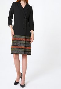 Svart blazerklänning med skräddarsydd passform, som har fyra knappar, trekvartslånga ärmar och en flerfärgad texturerad nederkant i orange, grönt och svart.