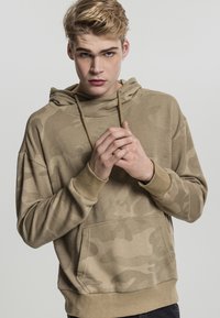 Beige hettegenser med camouflagemønster, med kengurulomme og ribbestrikkede mansjetter. Myk tekstur og avslappet passform.