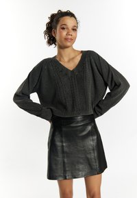Dunkelgrauer, gestrickter Pullover mit V-Ausschnitt und strukturiertem Muster, kombiniert mit einem schwarz-lackierten, hoch-taillierten Minirock aus Leder.