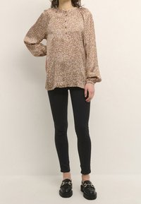 Brown patterned blouse with pink spots, button closure, and puffed sleeves, paired with black skinny jeans and black loafers.