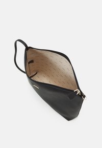 Czarna torba z ekoskóry o wyraźnym kształcie, z zamkiem błyskawicznym i beżowym wnętrzem z markowym podszyciem. Pojedynczy uchwyt.