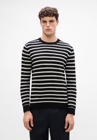 Suéter de rayas blanco y negro con cuello redondo, mangas largas y puños de canalé. Hecho de una tela suave y texturizada.