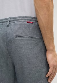 Grau linnenartige Hosen mit glatter Textur, elastischem Bund und einer Gesäßtasche mit rotem Etikett.