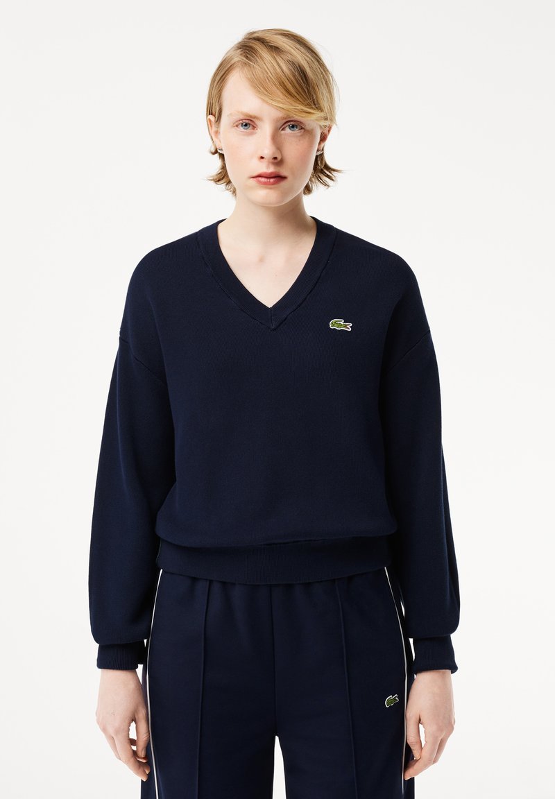 Marineblauwe V-hals fleece trui met lange mouwen, geribbelde manchetten en zoom; heeft een klein groen krokodillenlogo op de borst.