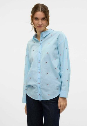 Camicia azzurro chiaro con ricami floreali rossi, maniche lunghe, texture morbida, colletto a punta, vestibilità casual.