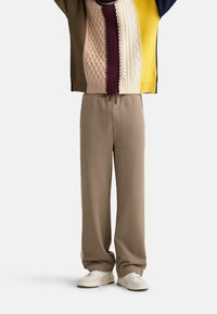 Pantaloni beige a quadri con una vestibilità comoda, vita elastica e tasche laterali. Indossati con un maglione a maglia multicolore e sneakers bianche.