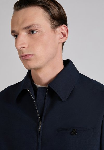 Navy blue zip-up jacket with a classic collar, featuring a small chest pocket and a smooth textured fabric. Simple, tailored design.