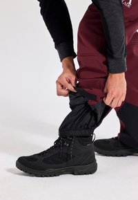 Vattentåliga maroonbyxor med justerbara svarta muddar, i kombination med svarta vandringskängor med strukturerade sulor och snörningsdesign.