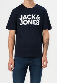 Camiseta de algodón azul marino de manga corta, con el gran texto blanco "JACK & JONES" en la parte frontal. Corte casual, textura suave.