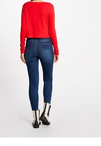 Röd långärmad kort topp kombinerad med mörkblå smala jeans. Modellen bär svartvita ankelboots med tjock klack.