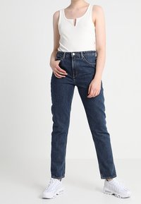 Top de tirantes blanco con cuello en V, combinado con jeans de tiro alto de color azul oscuro y zapatillas blancas. Silueta simple y ajustada.