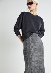 Hanorac gri cu accente din mărgele și fustă lungă gri tricotată, cu un model din tricot de tip cable knit. Modelul poartă ochelari de soare negri și un colier din lanț argintiu.