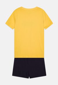 Camiseta de algodón amarilla con mangas cortas y un cuello redondo, combinada con pantalones cortos de color azul marino oscuro. Diseño sencillo, textura suave, sin patrones ni acentos.