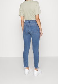 Högmidjade blå jeans med en figurnära passform. Tillverkade av denim, med bakfickor och en dragkedja med knäppning. Bärs med en ljus t-shirt.