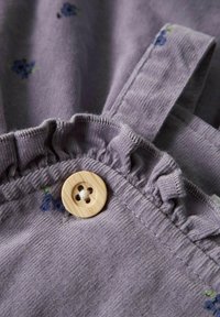 Grått stoff med ribbet tekstur, med små blå blomster. Volangdetaljer ved halsen og en rund treknapp.