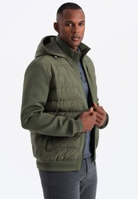 Olivgrön hooded jacka med quiltat övre, texturerade nedre sektioner och ribbade manschetter. Har dragkedjefickor och en stilren design.