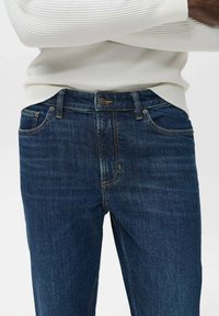Dunkelblaue Jeans im klassischen Schnitt mit einem Reißverschluss, Fronttaschen und Kontrastnähten. Der Stoff hat eine leichte Struktur.