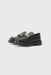Black leather loafers with a flat platform sole, featuring a wide strap and gold hardware detail on the front. Smooth texture.