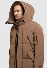 Hnedá puffová bunda s veľkou kapucňou, s horizontálnym prešívaním, zipsovými vreckami a predným zipsom. Hladká textúra látky.
