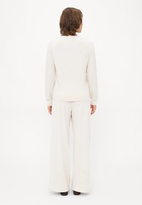 Suéter de punto beige claro con cuello redondo, mangas largas y dobladillo acanalado, combinado con pantalones de pierna ancha color crema.